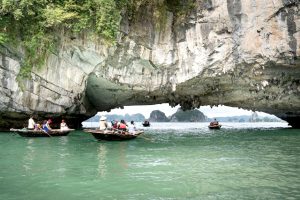 Tourists explore scenic Halong Bay in small boats under a limestone arch, surrounded by clear waters.